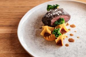 a plate with a piece of meat with cheese and broccoli at Corona Dolomites Hotel in Andalo
