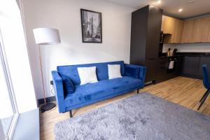 a blue couch in a living room with a kitchen at Modern Borehamwood Flat - 2 Min Walk to Station in Borehamwood