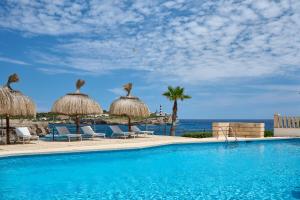 a swimming pool with chairs and umbrellas and the ocean at Orange Colom - Seaside Apartments in Portocolom