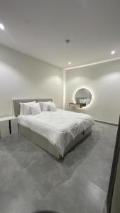 a white bedroom with a bed and a mirror at Royal Al Arfan Apartment in Muscat
