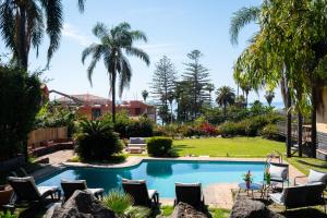 a swimming pool in a yard with chairs and palm trees at Silvanae Pool Villa in Aci Castello