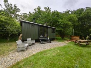 a green building with benches and a picnic table at Bell Nook- Shepherd's hut with a spacious wood-fired hot tub in Tonbridge