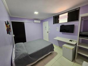 a bedroom with purple walls and a bed and a tv at Alice Suites in Arraial do Cabo