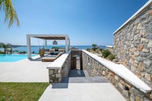 a stone wall next to a swimming pool and a villa at Elements Villas in Lartos