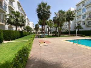 a walkway with palm trees and a swimming pool at Appartement de haut standing,4 piscines in Bouznika +5 photos