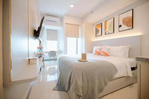 a white bedroom with a bed and a table at Pakuwon Mall Apartemen Anderson Orchard Tanglin Benson by AquHome in Surabaya