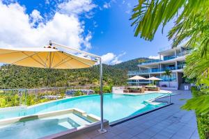 a swimming pool with an umbrella and a building at Seaviews at Searene, Spacious, Pool & Free WIFI in Airlie Beach