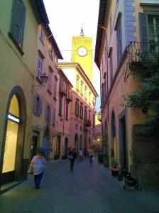 a woman walking down a street with a clock tower at Appartamenti Urbevetus in Orvieto
