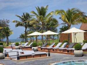 a row of lounge chairs and umbrellas next to a pool at voco Quang Binh Resort by IHG in Dong Hoi