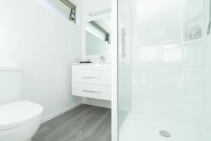 a white bathroom with a toilet and a shower at Banana Bungalow Studio in Raglan