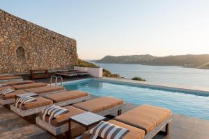 エリアビーチにあるCova Mykonos Suitesの壁の横に長椅子付きのスイミングプール