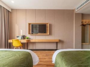 a hotel room with two beds and a desk with a television at GreenTree Inn Jining Jianshe Road Hotel in Jining