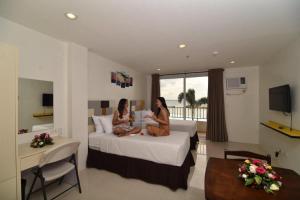 two women sitting on a bed in a hotel room at Holiday Oceanview Residences and Resort in Dasag
