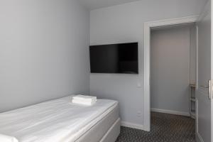 a white bedroom with a bed and a flat screen tv at Roze Park Rooms in Liepāja