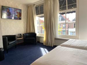 玛库姆Hotel DeWaag Makkum的一间带一张床、两把椅子和两扇窗户的酒店房间