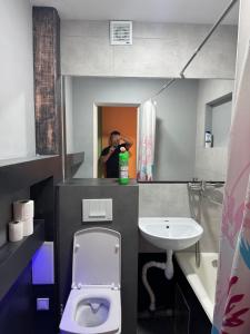 a man taking a picture of a bathroom with a toilet and sink at Aeroport apartament in Chişinău