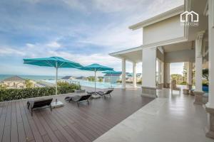 a patio with chairs and umbrellas and the ocean at DCAO Villas Novaworld Phan Thiet in Bình Tú