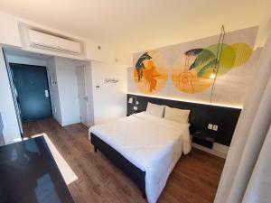 ein Schlafzimmer mit einem weißen Bett und einem Gemälde an der Wand in der Unterkunft ibis Styles Taubate in Taubaté