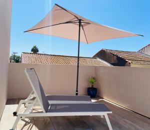 a chair and an umbrella on a balcony at L’écurie - Maison neuve 5 personnes, piscine in Portiragnes