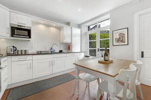 a white kitchen with a wooden table and white chairs at Roseberry Cottage in Ambleside