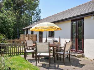 a wooden table with chairs and an umbrella at Columbine Cottage in Bude