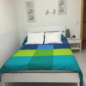 Una cama con una manta azul y verde. en Hostal Tres Cantos, en Tres Cantos