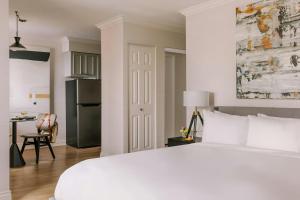 a bedroom with a large white bed and a kitchen at The Sunset Hotel West End in Vancouver