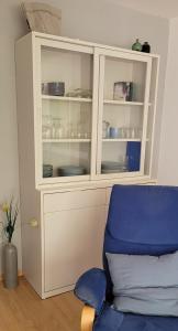 Un armario blanco con platos y una silla azul. en Waldstraße 2 Windrose Kellenhusen, en Kellenhusen