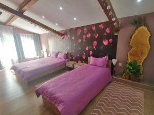 2 letti in una camera da letto con lenzuola viola e fiori sul muro di къща Горски чар a Beli Osam