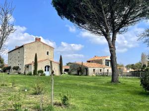 an old building in a field with a tree at Logis de la Vau - Private pool - Quiet in Saint-Benoist-sur-Mer