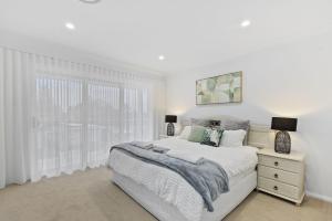 a white bedroom with a bed and a window at Brand New Beach House in The Entrance