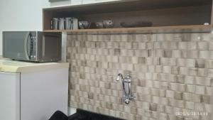 a kitchen with a microwave and a tile wall at Kitnet Mobiliada in Vitória da Conquista