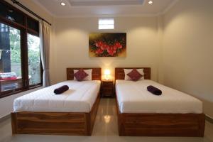 two beds in a room with a painting on the wall at KT. Kuaya Home Stay in Ubud