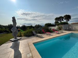a swimming pool with chairs and an umbrella next to it at Villa élégance et sérénité in Gignac
