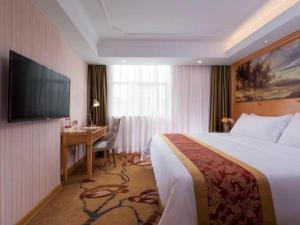 ein Hotelzimmer mit Bett, Schreibtisch und Fernseher in der Unterkunft Vienna Hotel Shenzhen Guanlan Shanshuitianyuan Xintian in Tiantangwei