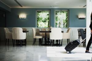 a person pulling a suitcase in a room with a table and chairs at Hotel Riviera & Maximilian's in Trieste