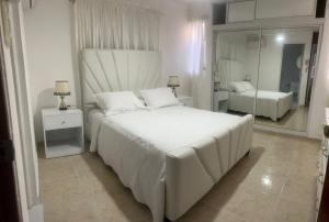 une chambre blanche avec un grand lit et un miroir dans l'établissement Casa de tres habitaciones con piscina, à La Romana