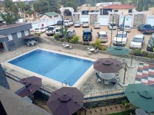 a swimming pool with umbrellas and a parking lot with cars at MK Hotel in Muisenge +8 photos