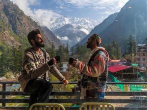two men are holding coffee cups in front of a mountain at The Hosteller Kasol, Parvati Valley in Kasol +22 photos