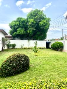 a green yard with a white wall and a tree at Refined Comfort at the Right Price-Four Bedroom Luxury Apartment in Accra