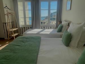two beds in a hotel room with a view of the ocean at Hôtel De La Marine in Arromanches-les-Bains