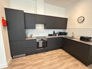 une cuisine avec des armoires noires et une horloge murale dans l'établissement Luxury 2 bedroom 2 bathroom All ground floor centrally located - 1 Queen Street - Ashbrook Serviced Apartments, à Abingdon