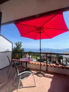a red umbrella on a balcony with a table and a chair at View point rooms in Matulji