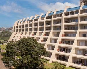 a large white building with a tree in front of it at Ocean View Family Apartment - L'Escalier 208 a ABR3 Haven in Amanzimtoti