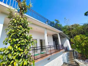 a white house with a balcony and a tree at Robin's Paradise Deluxe Villa in Vagamon