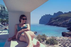 a woman sitting on a balcony with a view of the beach at El Vicenç de la Mar - Adults Only - Over 12 in Pollença