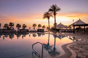 a swimming pool with palm trees and a sunset at Coral Beach Hotel & Resort Cyprus in Coral Bay