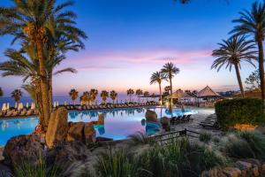 a resort pool with palm trees and chairs at Coral Beach Hotel & Resort Cyprus in Coral Bay