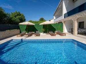 a swimming pool with chairs and umbrellas next to a building at Holiday Home Domagoj by Interhome in Malinska