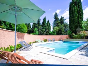 a swimming pool with chairs and a green umbrella at Holiday Home Mas des Lavandes by Interhome in Graveson